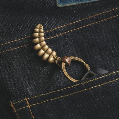 Close-up of a golden metallic dragon keychain tail in a denim pocket.