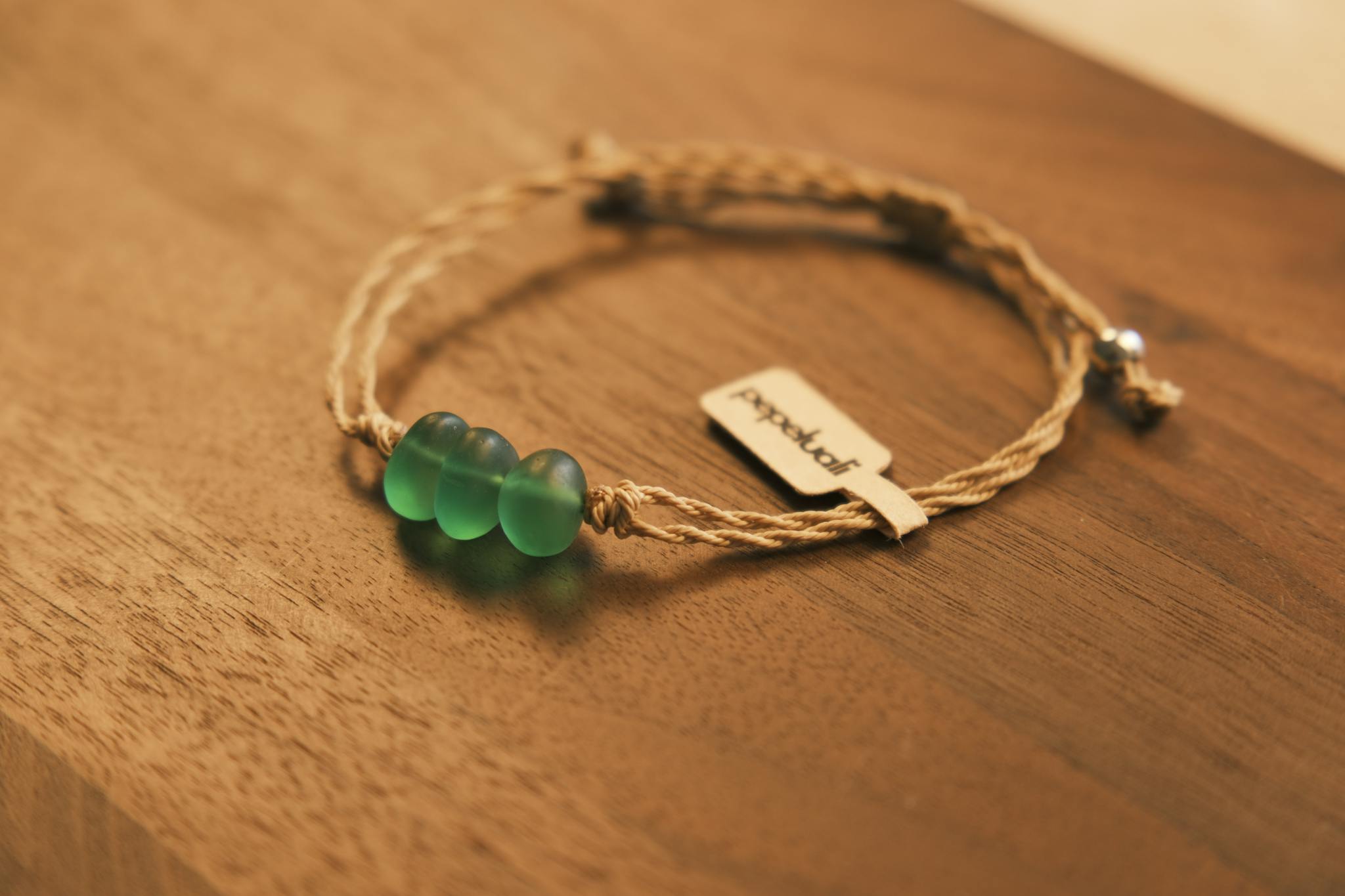 Close-up of a handcrafted bracelet with green glass beads on a wooden table.